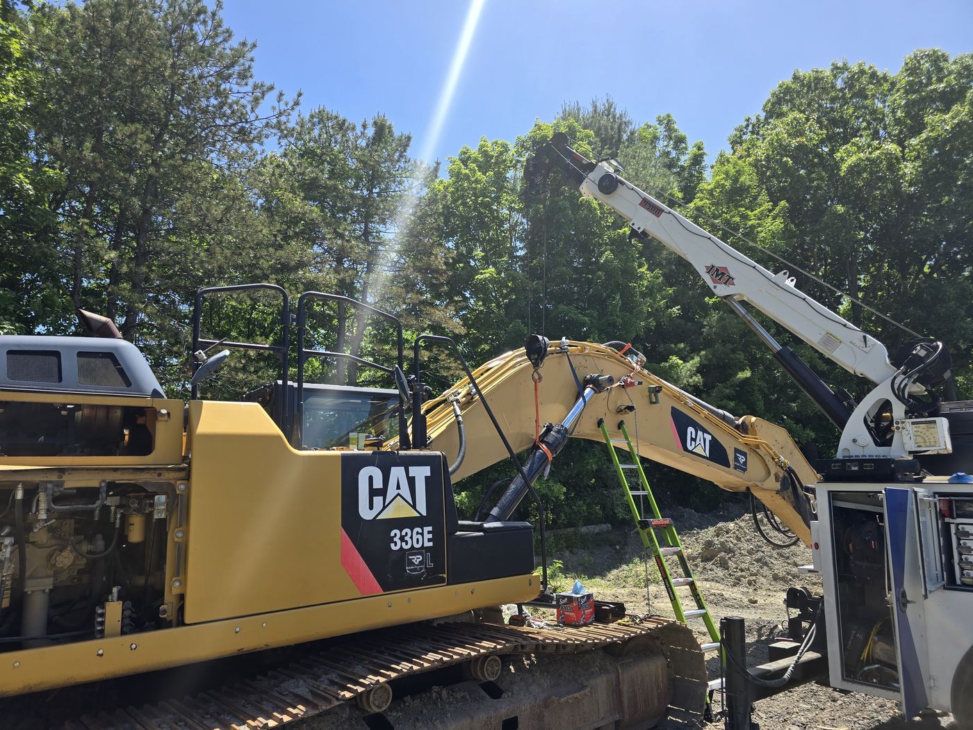 Boom truck holding the arm of an excavator while Jake Decker performs a field repair